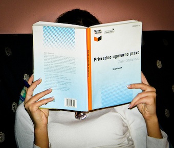 Study time by Stanković Vlada A female student reading a Serbian contract law book, her face is obscured by the book